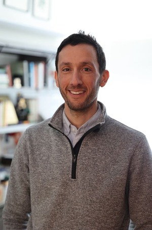 professor wearing a gray zip up sweater in front of a bookcase